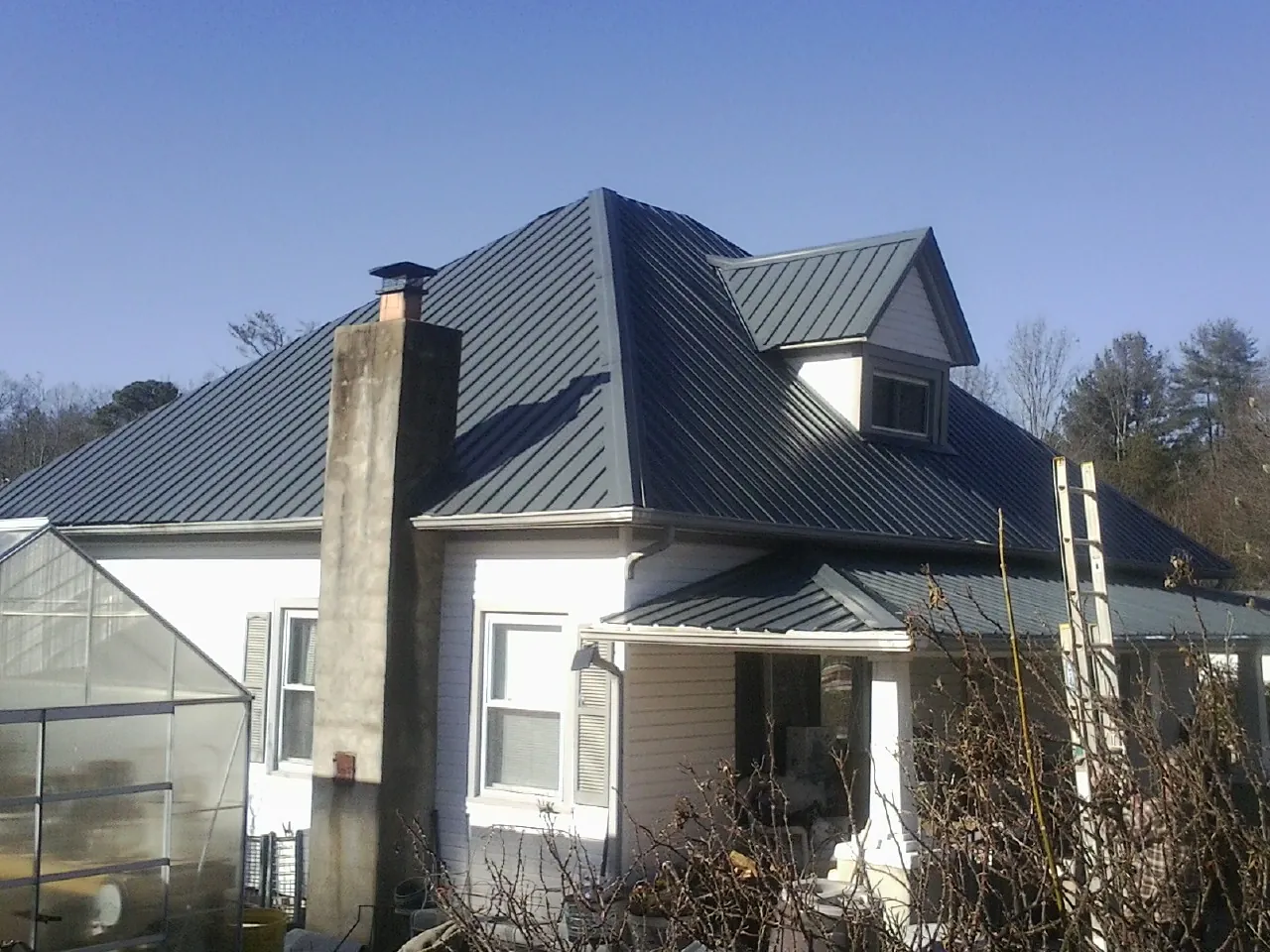 Dark blue standing seam metal roof on a white farmhouse with dormer — Slate & Tile Roof Repair by Roofing Brothers in Beemer