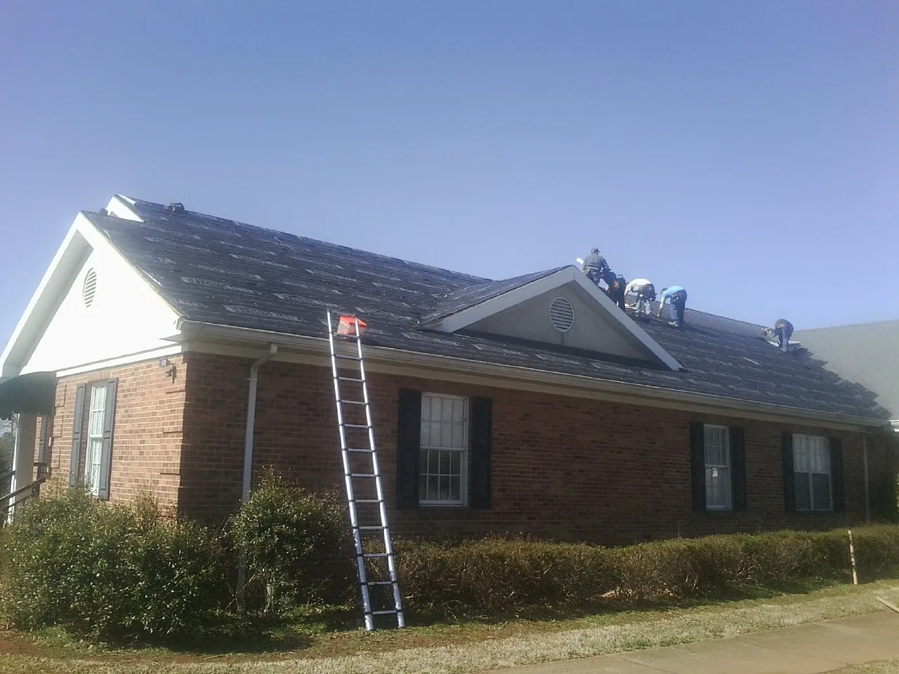 Crew tearing shingles off a brick ranch roof with a ladder set — Emergency Roof Repair work by our crew in Beemer