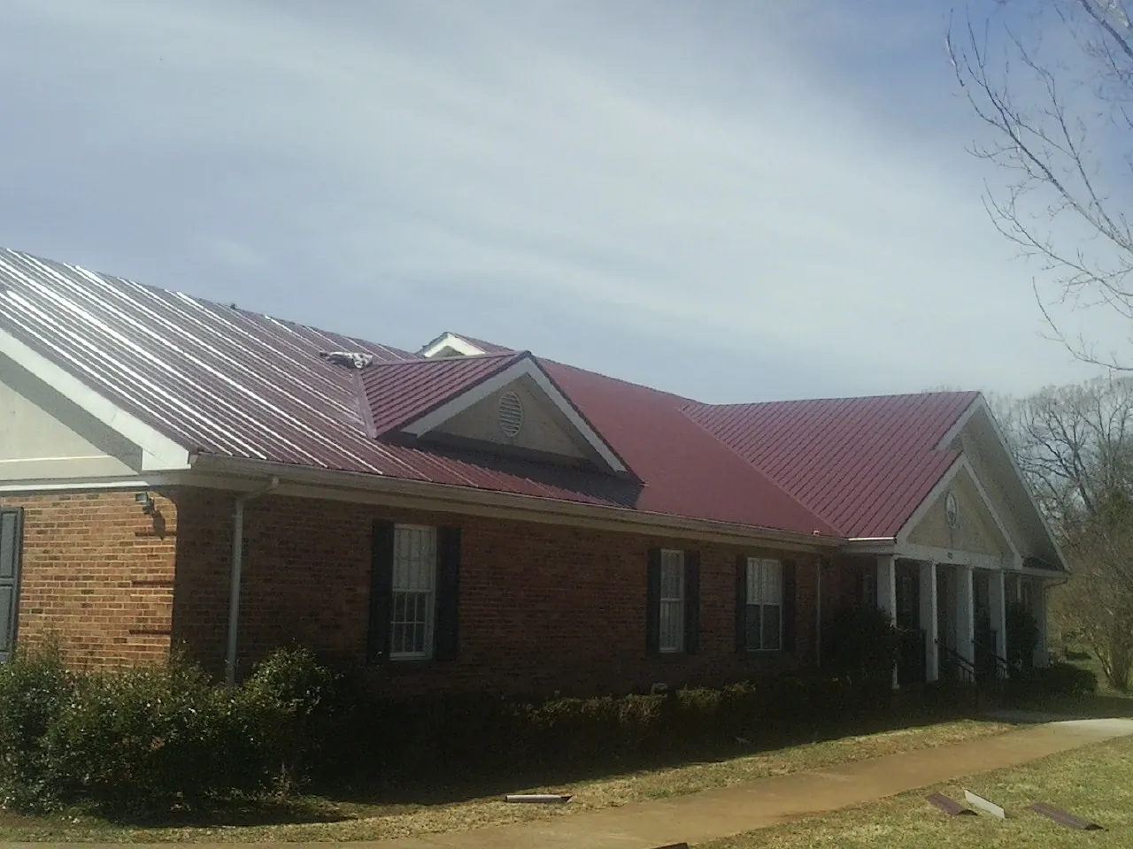 Red metal roof with gabled entries on a long brick building, from a Hail Damage Roof Repair job in Beemer