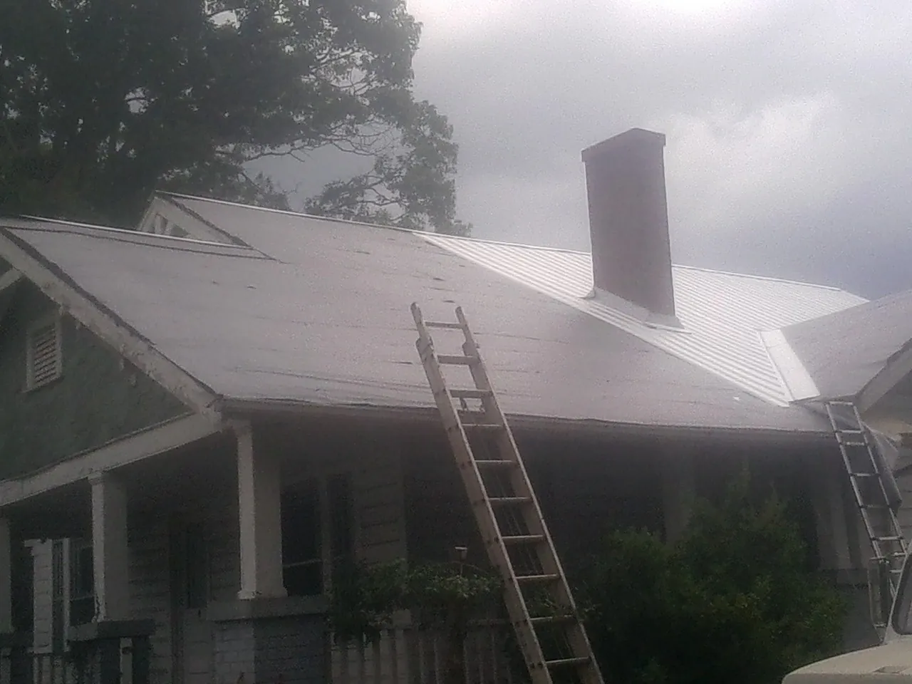 Ladders against a metal roof on an older home with a brick chimney in Beemer