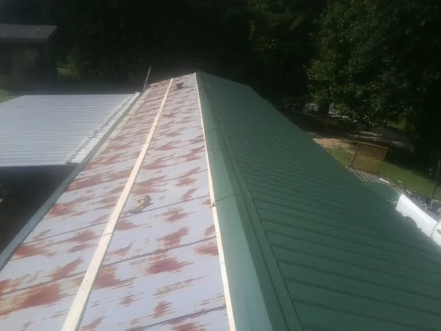 Old rusted panels beside newly installed green metal roofing — Wind Damage Roof Repair by Roofing Brothers in Beemer