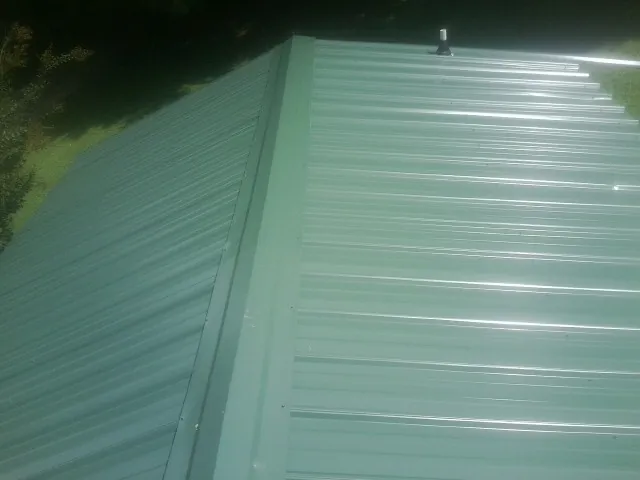 New green metal panels meeting at the ridge of a roof — Flat Roof Repair work by our crew in Beemer