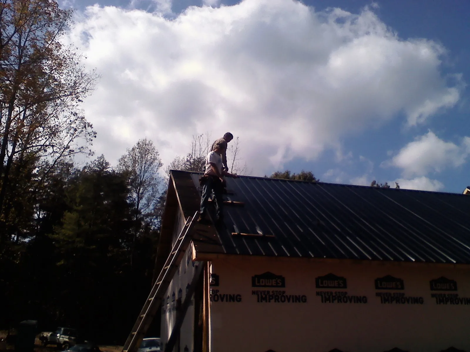 Roofer fastening dark metal panels high against a cloudy sky, from a Roof Inspection job in Beemer