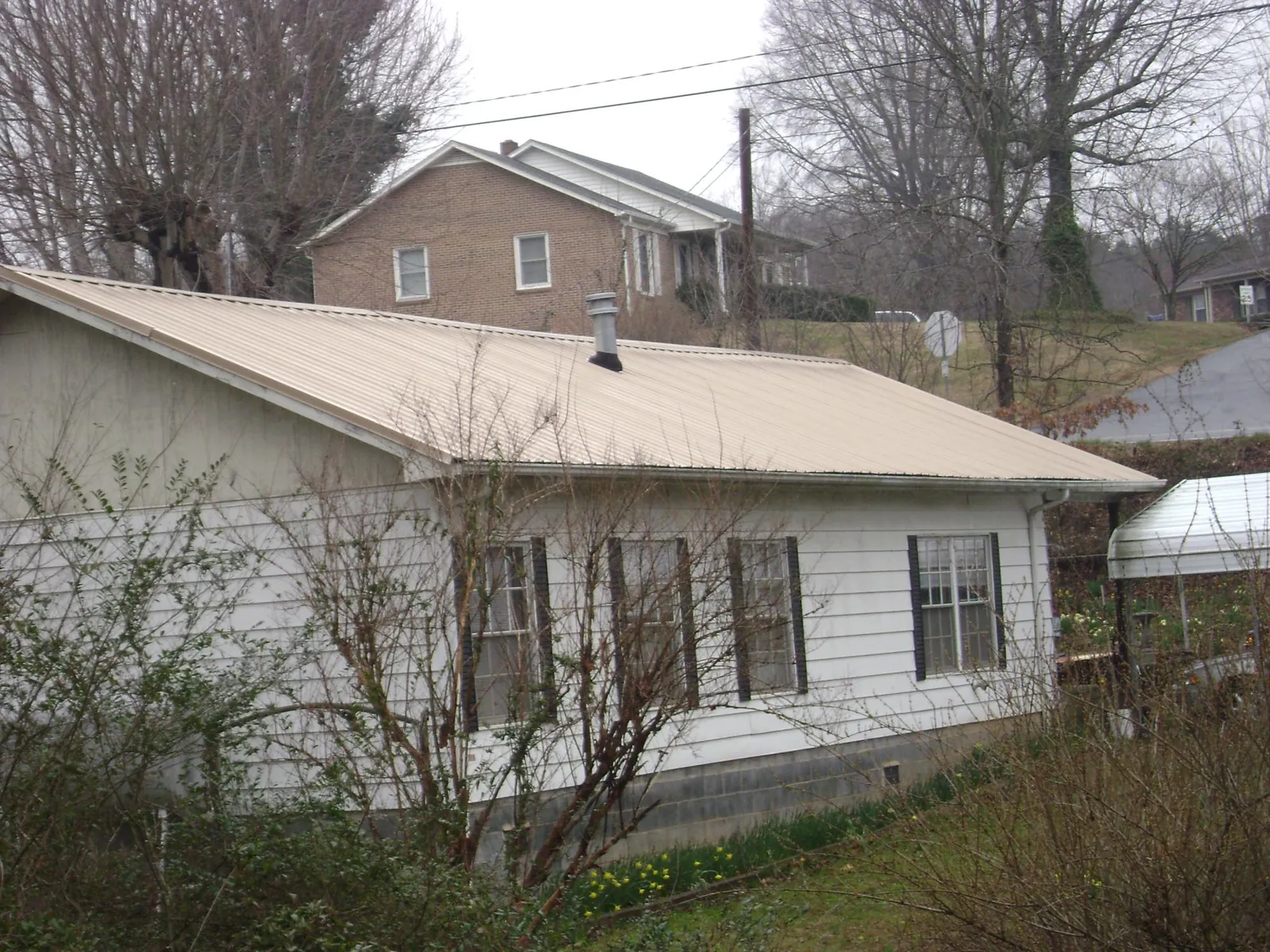 Tan metal roof on a white sided house set into a hillside — Commercial Roofing by Roofing Brothers in Beemer