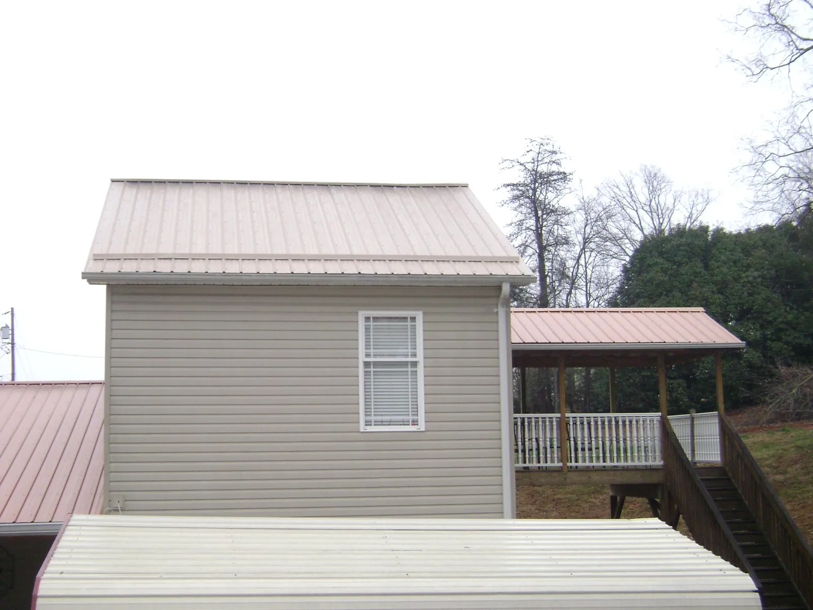 Tan metal roofs on a two story addition and attached porch, from a Roof Replacement job in Beemer